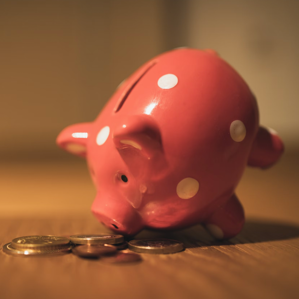 A pink piggy back leaning forwards with its snout on some coins